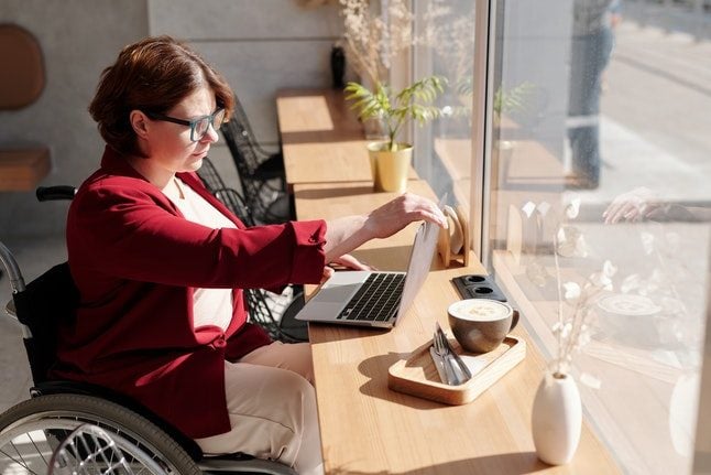 Woman in wheelchair on laptop in cafe