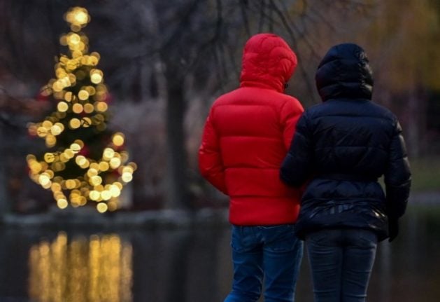 A couple stand next to a pond with a glowing Christmas tree at the Stadtpark (City park) in Vienna